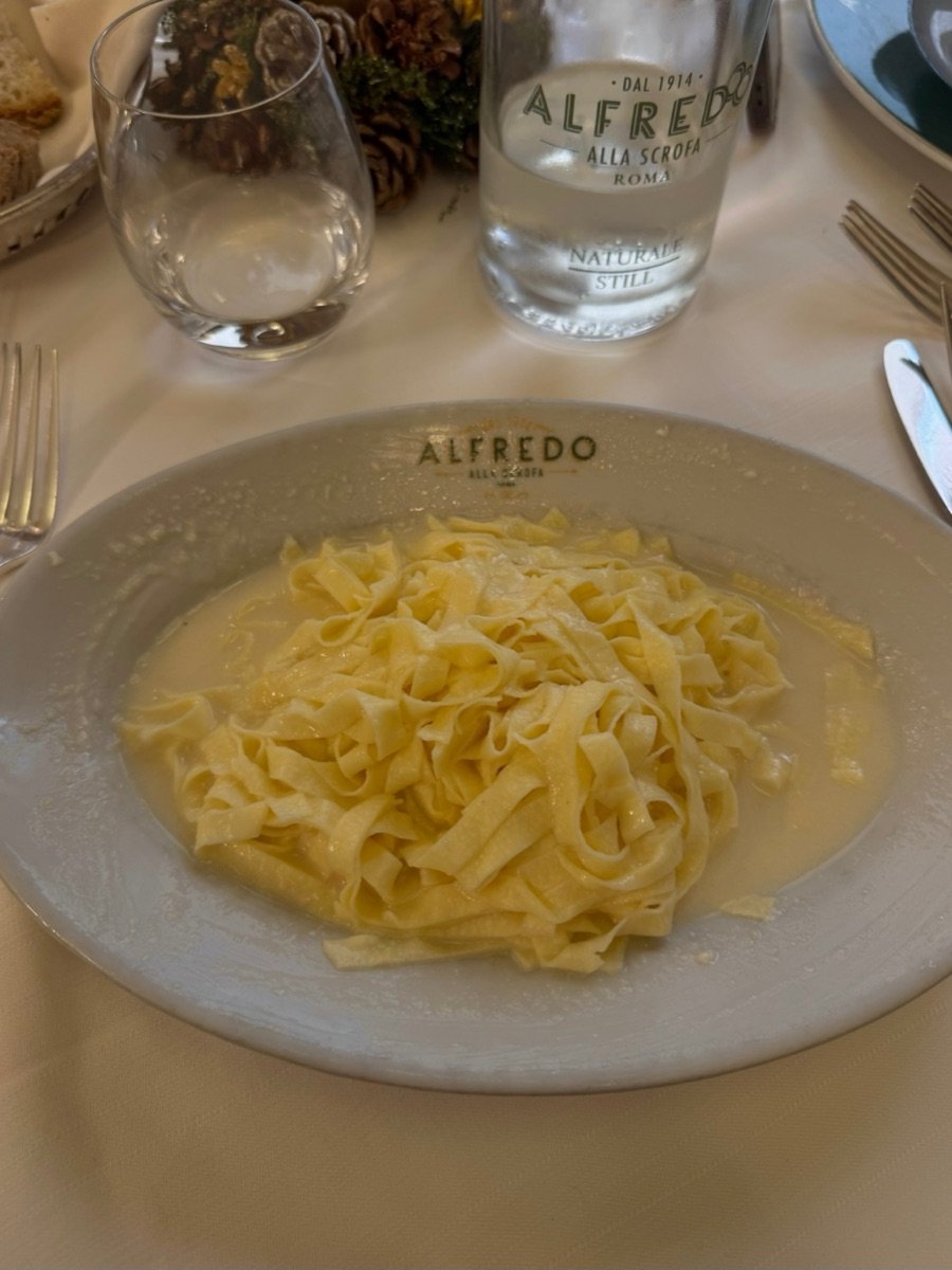 Fettuccine Alfredo turned in butter and parmesan, served on a pale plate stamped with the restaurant&rsquo;s name.