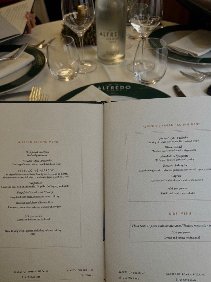 The open tasting menu laid across a set table, glasses and cutlery and a green napkin embroidered Alfredo on either side.