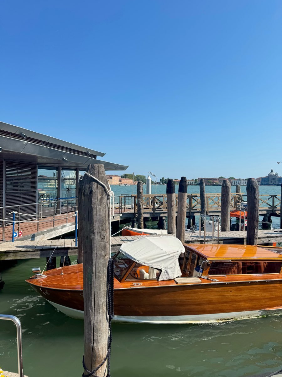 A varnished wooden water taxi moored at a jetty beside weathered mooring posts.