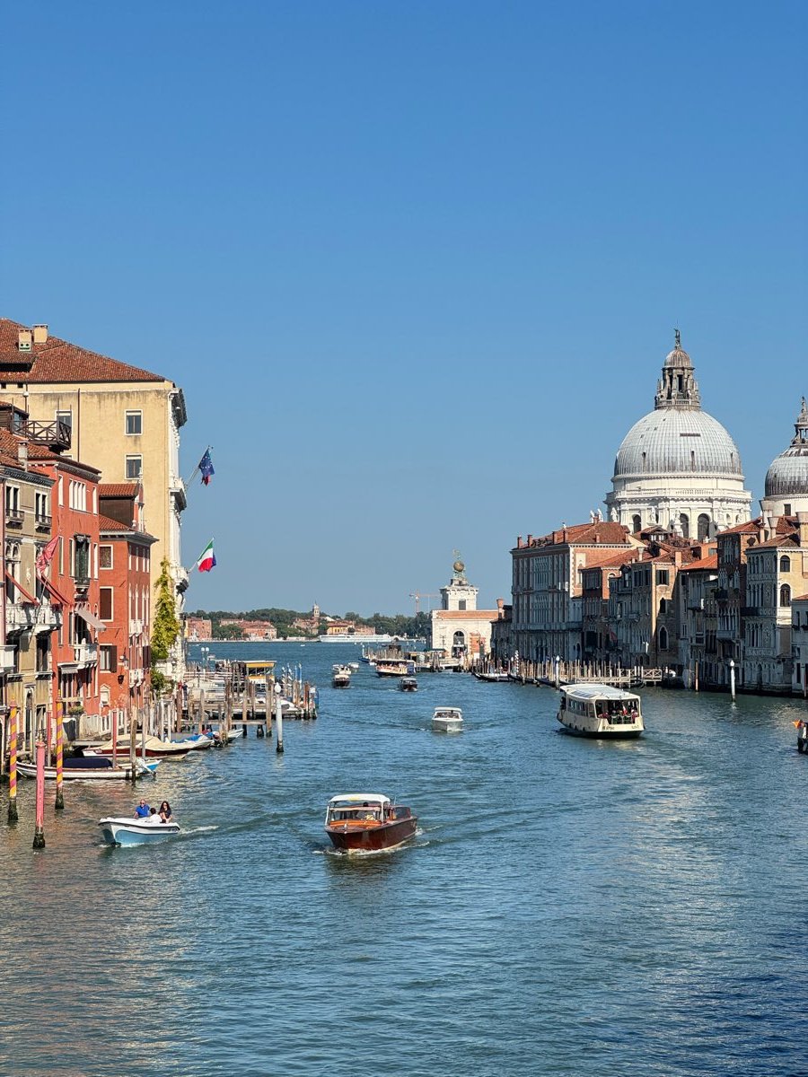 A wide canal seen from a bridge, lined with pale buildings and busy with small boats, a domed church closing the view.